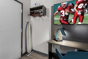 Une pièce équipée d’un téléviseur diffusant un match de football, d’un porte-manteau, d’un bureau et d’une chaise.