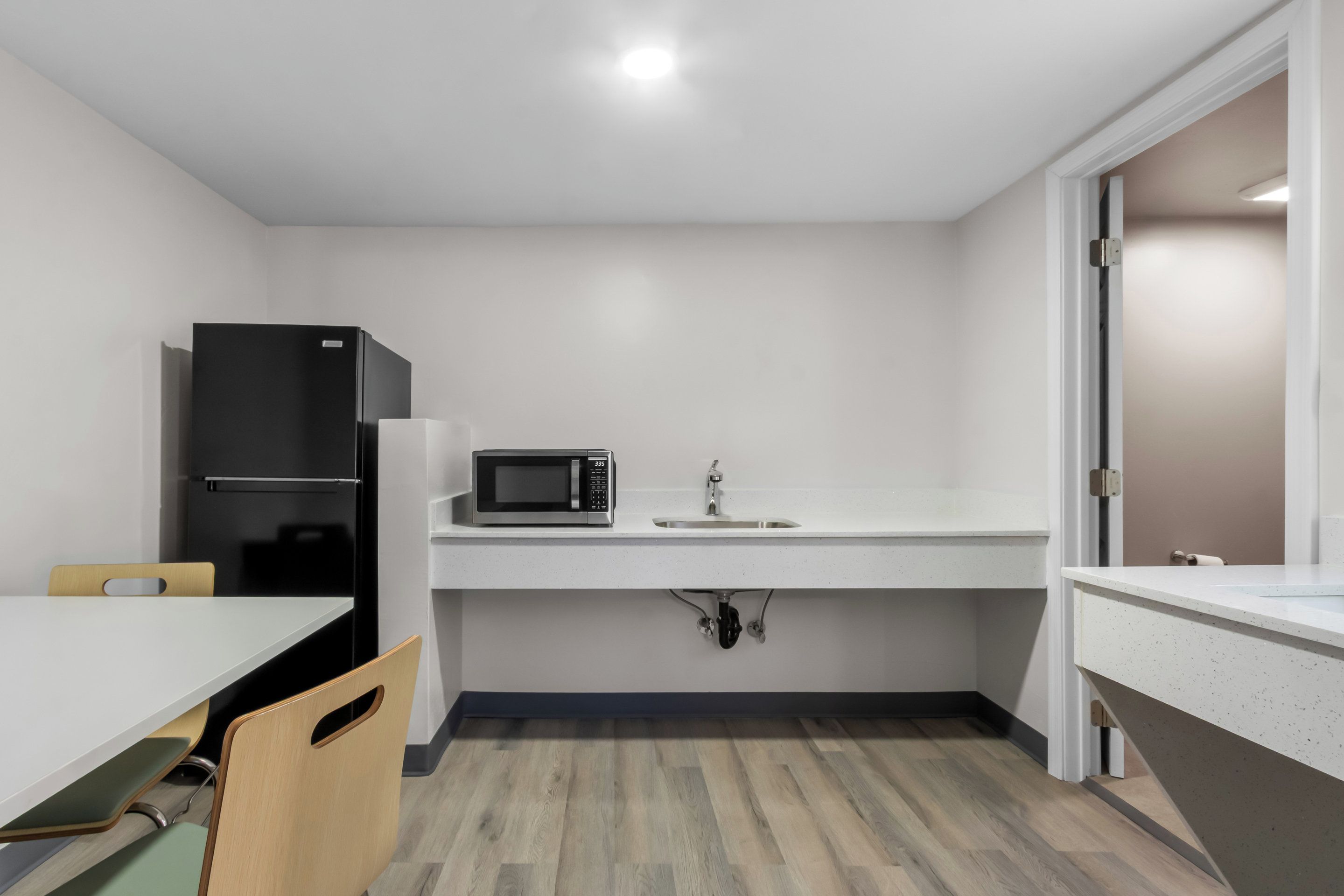 A compact kitchen with a refrigerator, microwave, sink, and wooden chairs.