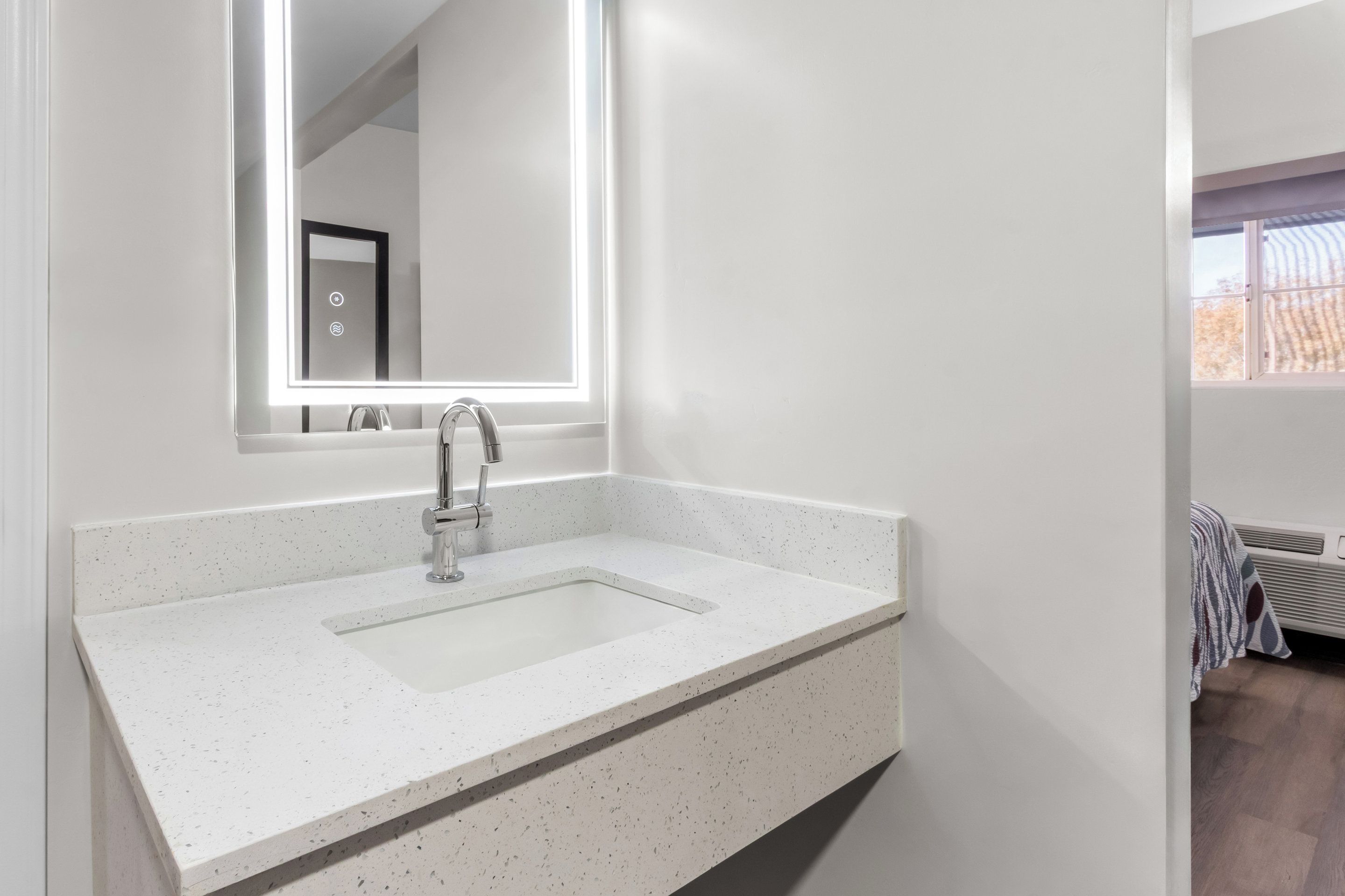A modern bathroom with a white sink, a large mirror, and a window providing natural light.