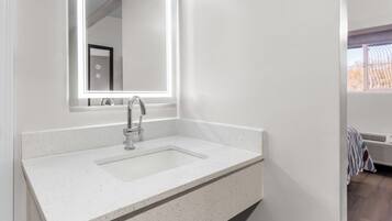 A modern bathroom with a white sink, a large mirror, and a window providing natural light.