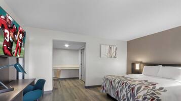 A modern hotel room with a bed, desk, and chair. There is a television on the wall displaying a sports game.