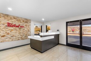 Balcão de recepção do Red Roof Inn com parede de pedra ao fundo, uma janela grande e vista para um estacionamento.