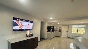 Una cocina moderna con un televisor de pantalla plana mostrando un anuncio de limpieza, un horno empotrado y una ventana con persianas.
