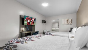 A hotel room with two beds, a TV, a desk, and a mirror.