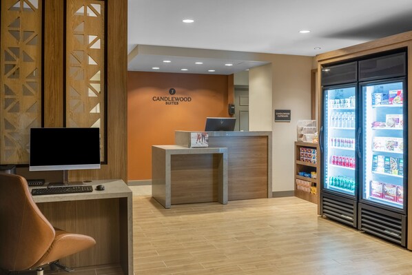 Zona de recepción con mostrador, computadora y refrigerador lleno de bebidas.