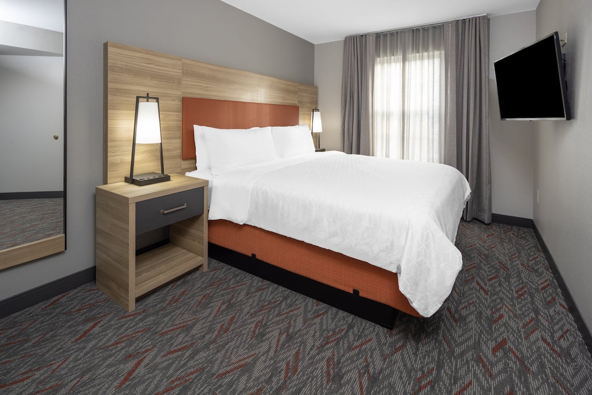 Ein Hotelzimmer mit Bett, Nachttisch, Lampe, Fernseher und Spiegel.