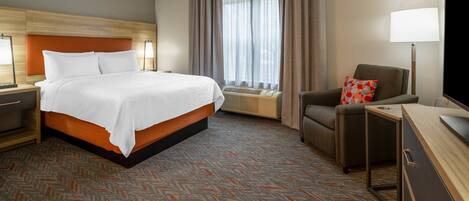 A hotel room with a bed, a chair, a desk, a lamp, and a window with curtains.