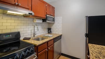 A kitchen with wooden cabinets, a stainless steel stove, a microwave, a dishwasher, and a black refrigerator.