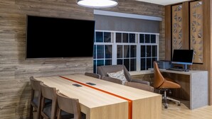 A modern office space with a large wooden desk, multiple chairs, a computer desk with a monitor, and a large window with blinds. - Candlewood Suites Boston North Shore Danvers by IHG (Danvers)
