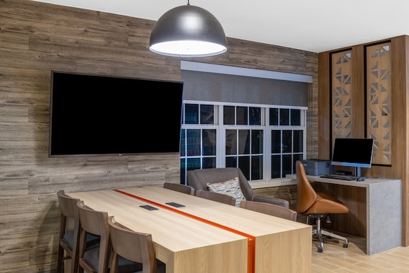 Un espacio de oficina moderno con un amplio escritorio de madera, varias sillas, un escritorio con computadora y monitor, y un gran ventanal con persianas.