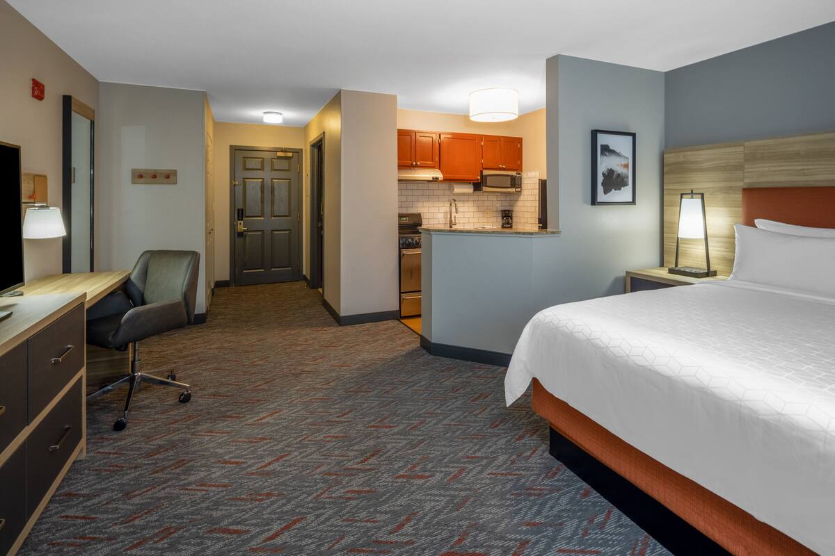 Ein Hotelzimmer mit Bett, Schreibtisch, Stuhl, Küchenzeile und einem zur Tür führenden Gang.