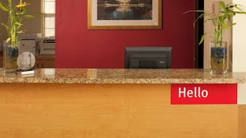 A reception desk with a red wall, a framed picture, and two potted plants.