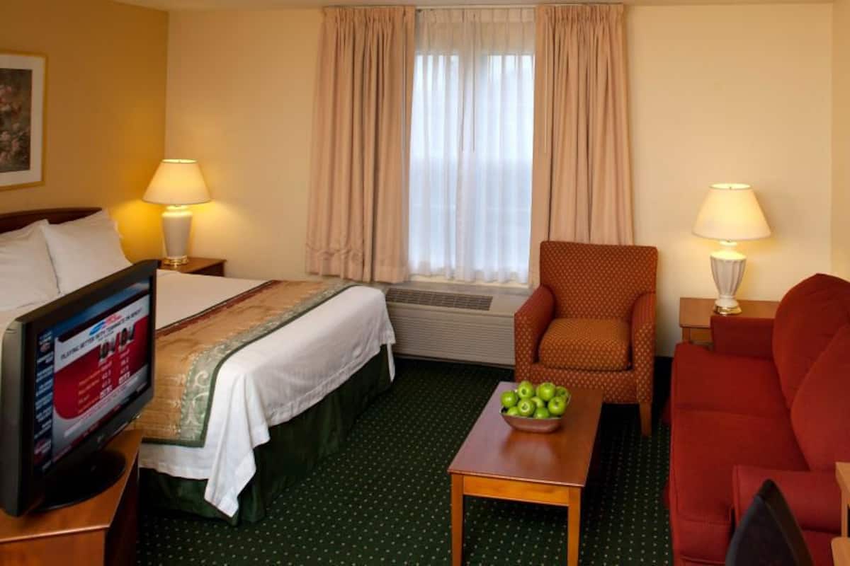 Une chambre d’hôtel avec un lit, une télévision, une table basse avec des pommes, un canapé rouge et un fauteuil.