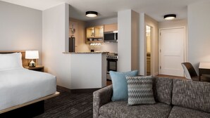 Ett hotellrum med en säng, en soffa, ett litet kök och en separat matplats.