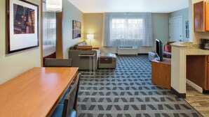 Een moderne hotelkamer met een houten eettafel, een bank, een klein bureau, een flatscreen televisie en een kitchenette met een magnetron en koffiezetapparaat.