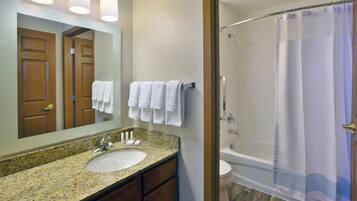 A bathroom with a granite countertop sink, a mirror, and a shower with a curtain.