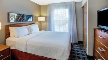 A hotel room with a bed, a television, a nightstand, and a window with curtains.