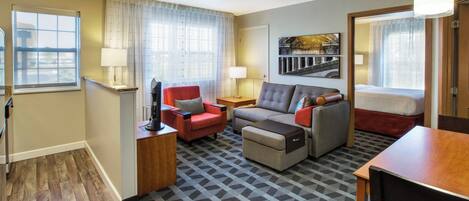 Una habitación de hotel con sofá, sillón, reposapiés, cama, escritorio y lámpara.