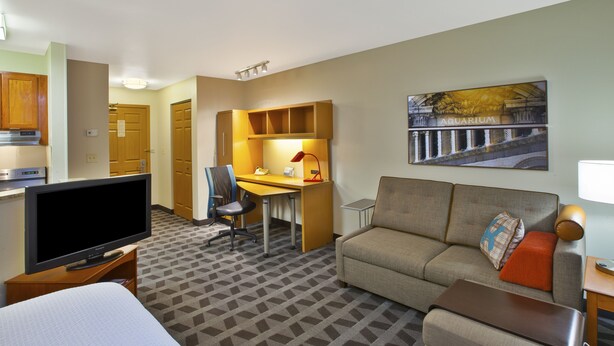 Hotelkamer met een bed, een televisie, een bureau met stoel, een bank en een schilderij van een aquarium.