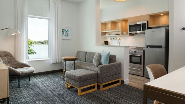 A modern living room with a sectional sofa, a dining table, and a kitchen area with a microwave, oven, and refrigerator.