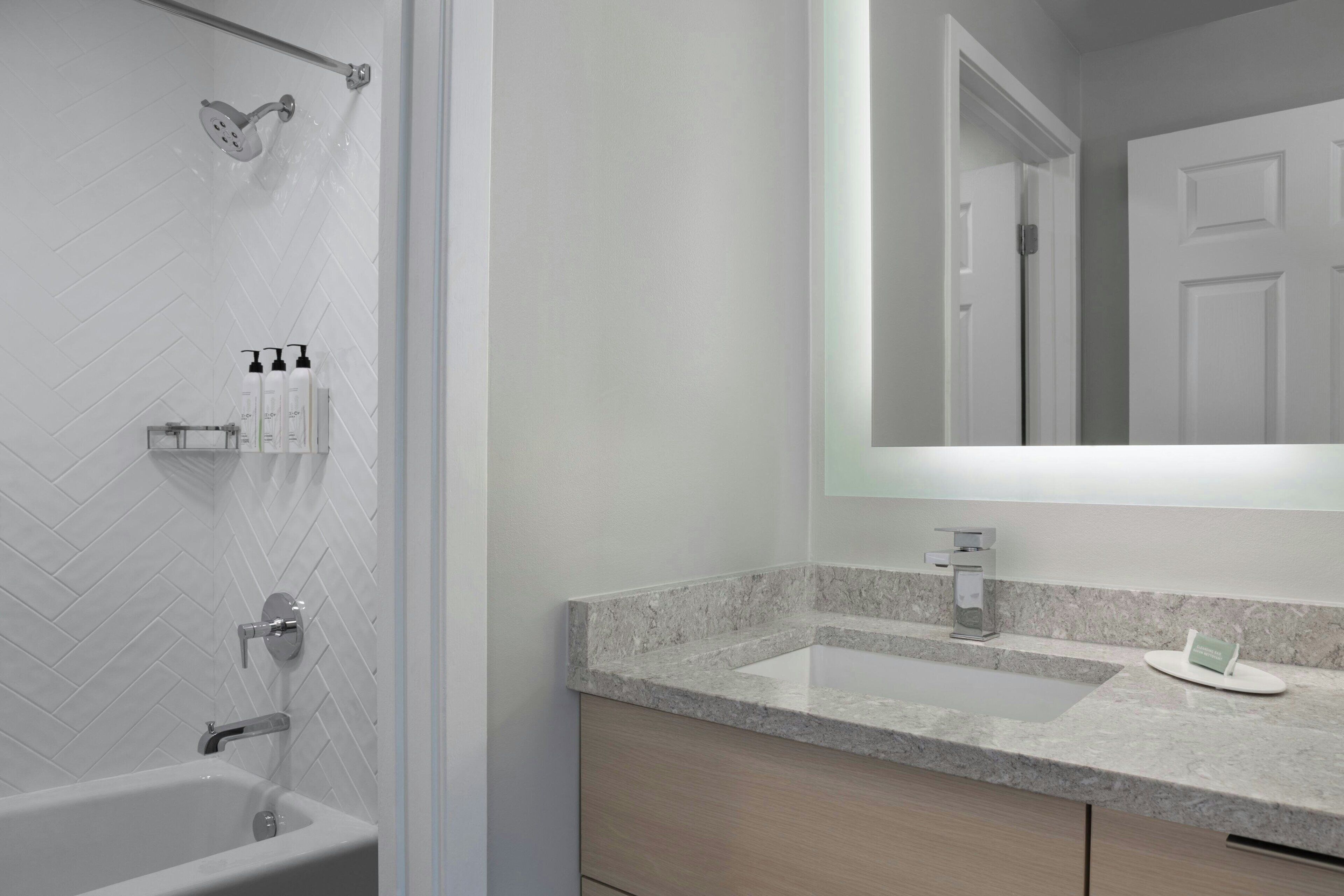 A modern bathroom with a freestanding bathtub, a large mirror, and a countertop with a sink and soap dispenser.
