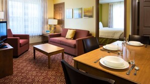 A hotel room with a red sofa, a wooden dining table set for two, a television, and a patterned carpet. - Sonesta Simply Suites Phoenix Scottsdale (Scottsdale)