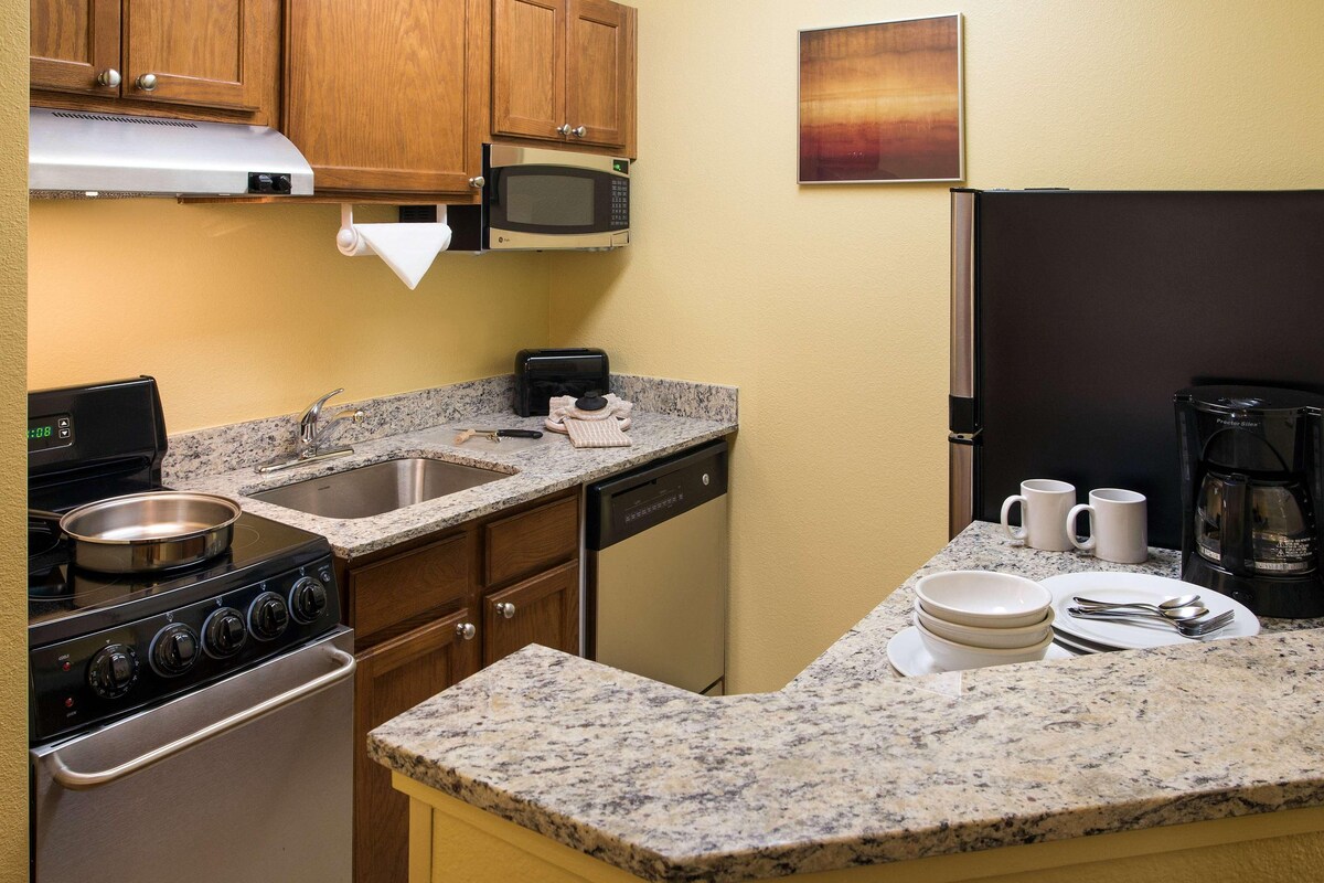 A compact kitchen with granite countertops, a stove, a microwave, a dishwasher, and a refrigerator.