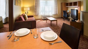 Ett hotellrum med en matplats, en soffa, en TV och ett fönster med gardiner.