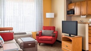 A hotel room with a sofa, armchair, TV, and a small kitchenette.