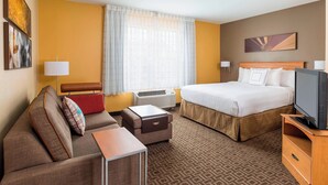 A hotel room with a bed, a sofa, a TV, a desk, and a window with curtains.