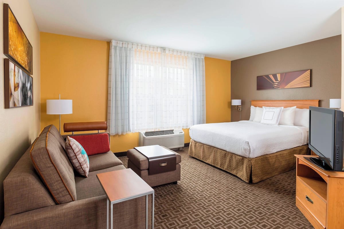 A hotel room with a bed, a sofa, a TV, a desk, and a window with curtains.