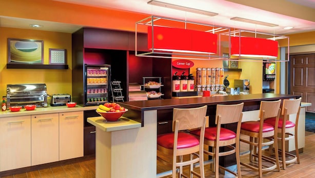 A modern kitchen area with a central island, bar stools, a refrigerator, a coffee machine, and a vending machine.