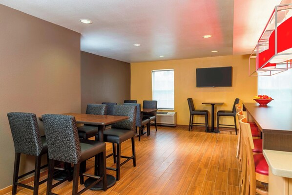 A dining area with wooden tables and chairs, a flat-screen TV mounted on the wall, and a window providing natural light.