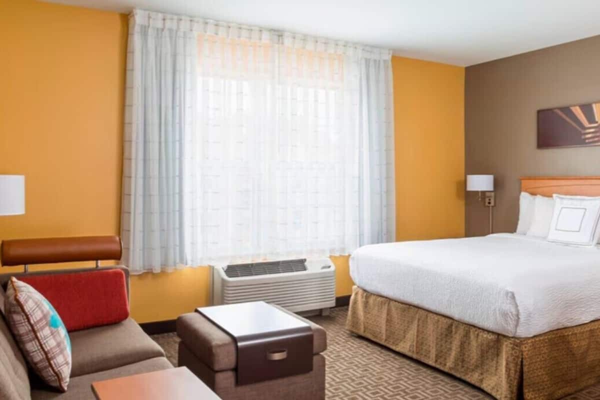 A hotel room with a large bed, a sofa, a small table, and a window with curtains.