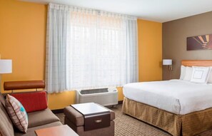 Habitación de hotel con una cama grande, un sofá, una mesita y una ventana con cortinas.