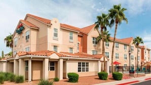 A hotel with a beige facade, red-tiled roof, and palm trees.