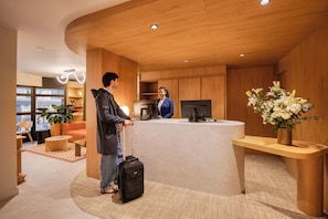 Un hall d’hôtel moderne avec un comptoir d’accueil, des panneaux de bois, une grande plante et un coin salon comprenant un canapé et une table basse.