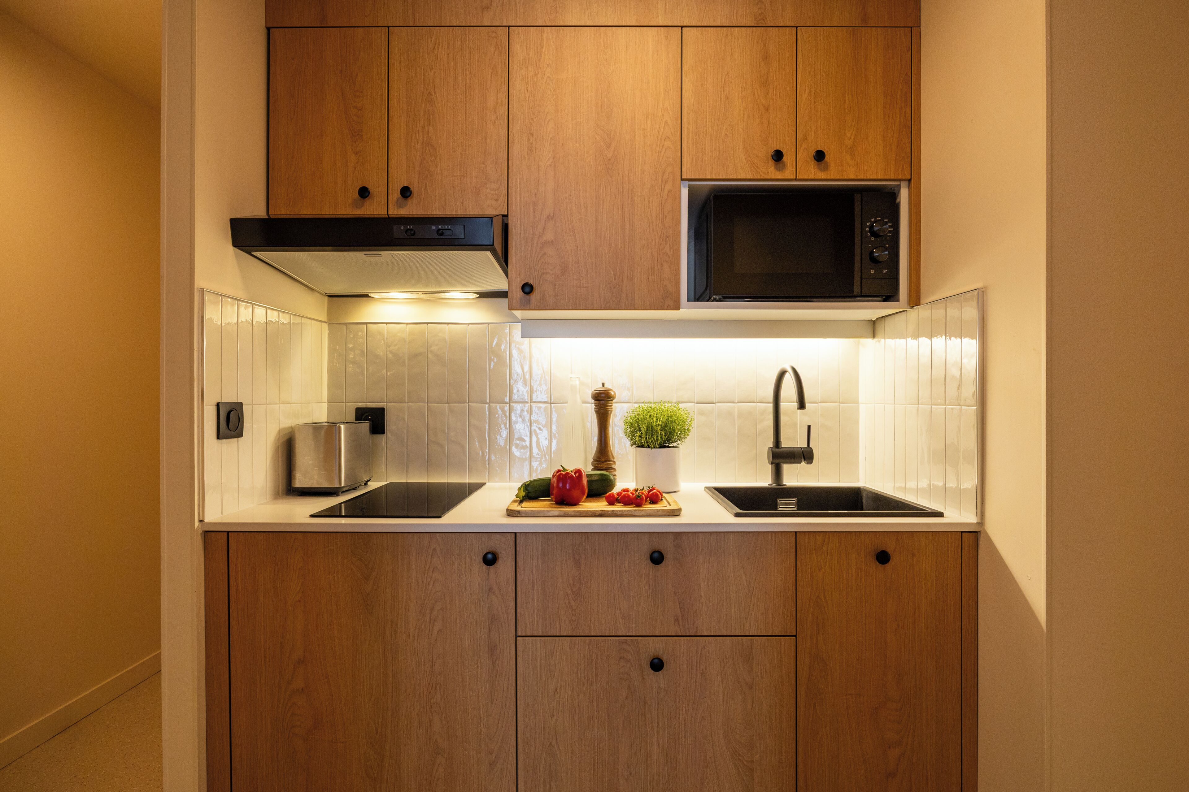 Eine kleine Küche mit Holzausstattung, einer Mikrowelle, einem Toaster und einem Spülbecken.