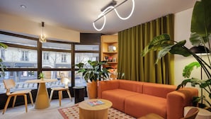 A modern living room with a sofa, chairs, a coffee table, and a bookshelf. - Citadines République Paris (Paris)