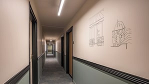 A hallway with a carpeted floor, doors on both sides, and a wall with a line drawing of a building and a couple. - Citadines République Paris (Paris)