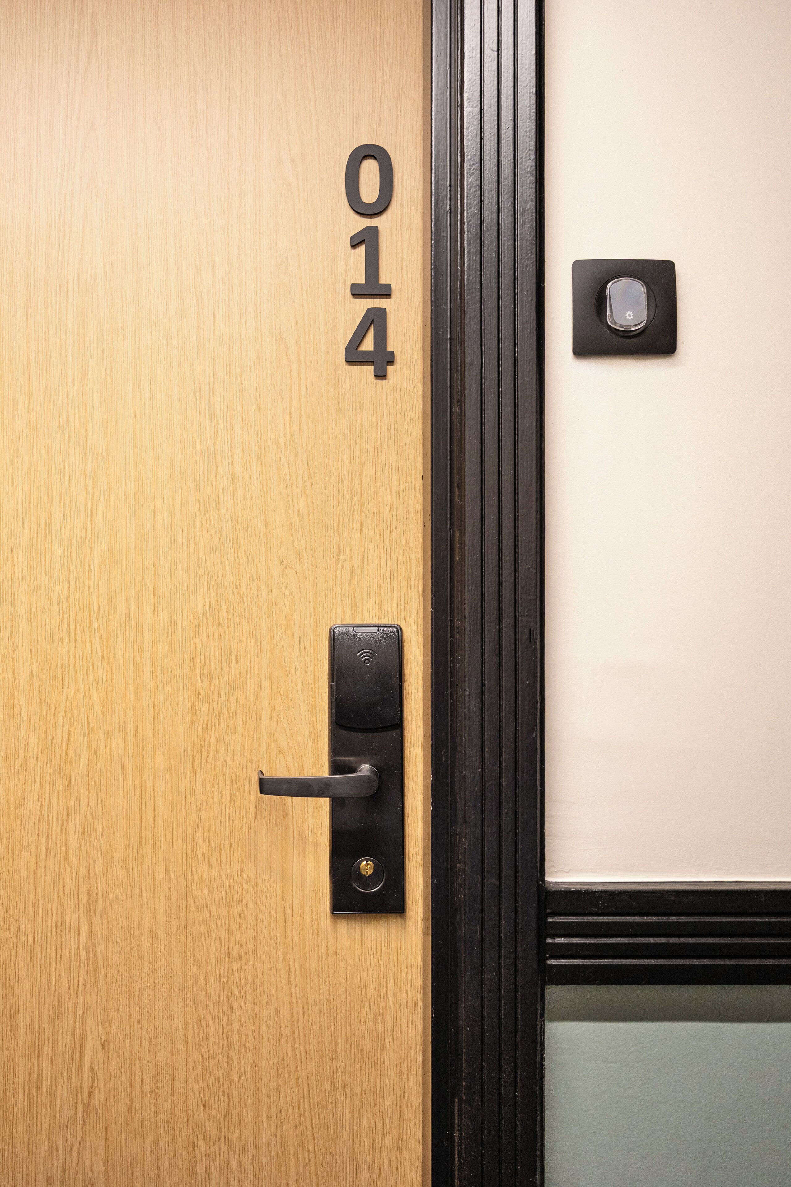 A wooden door with the number 014, a black door handle, and a small square object on the wall.