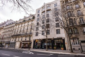Um edifício de vários andares com um café no andar térreo, grandes janelas e uma árvore em frente.