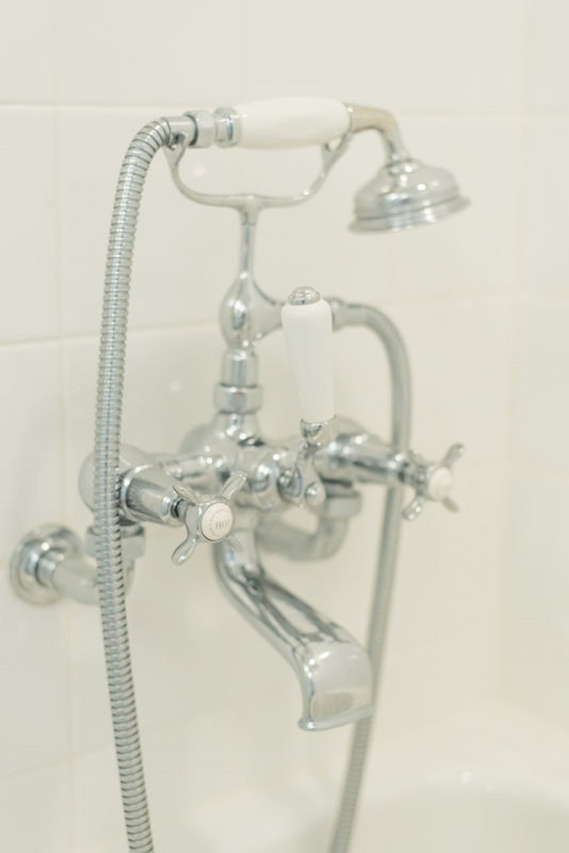 A bathroom with a chrome showerhead, a handheld shower, and a wall-mounted faucet.