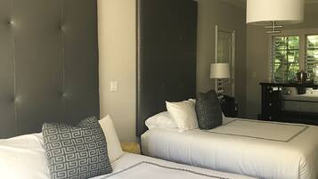 Une chambre d’hôtel avec deux lits, une grande tête de lit sombre, une table de chevet avec une lampe et une fenêtre avec des stores.