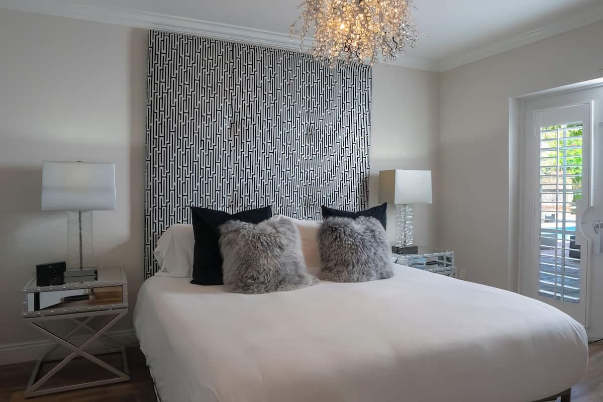 Quarto com uma cama grande, duas almofadas fofas, cabeceira estampada, abajures e um candelabro.