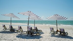 Des chaises de plage avec des parasols à rayures, sur une plage de sable, avec l’océan en arrière-plan.