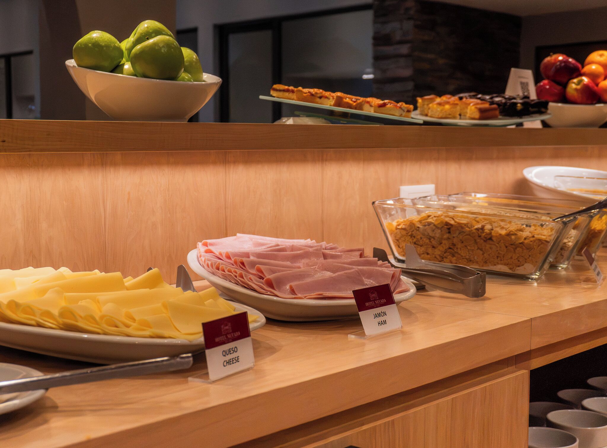 A buffet counter with various food items including ham, cheese, and a dish labeled 'JAMÓN HAM'.
