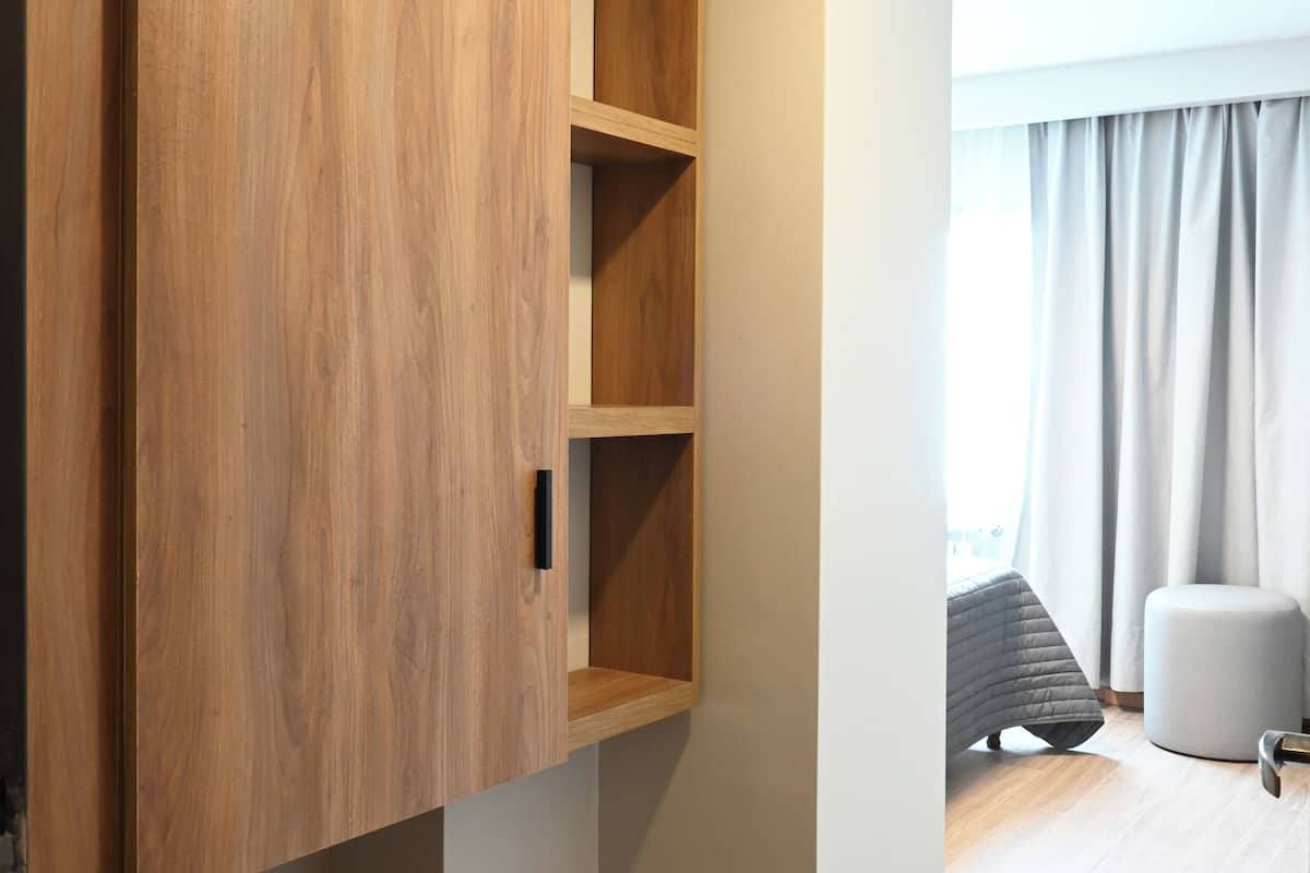 Een kamer met een houten garderobe, een grijze bank en een raam met gordijnen.