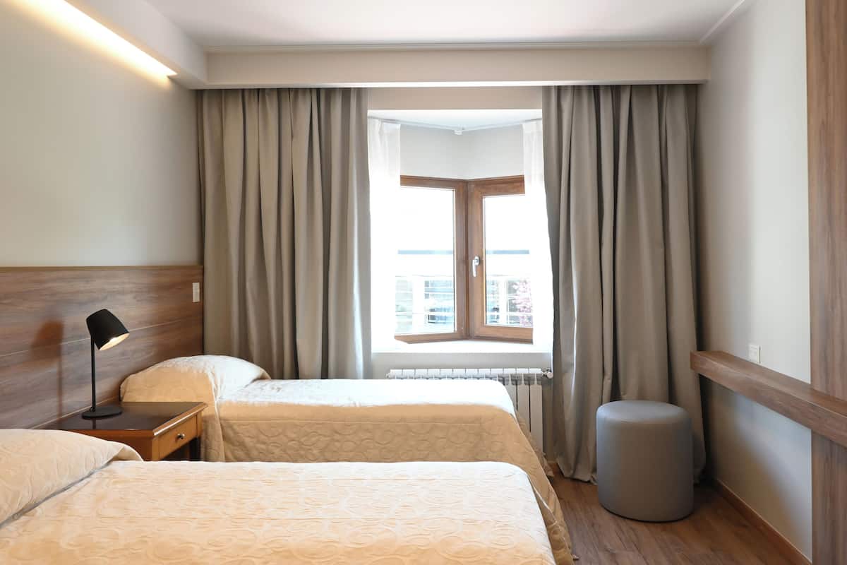 Een hotelkamer met twee bedden, een nachtkastje, een lamp, een raam met gordijnen en een radiator.