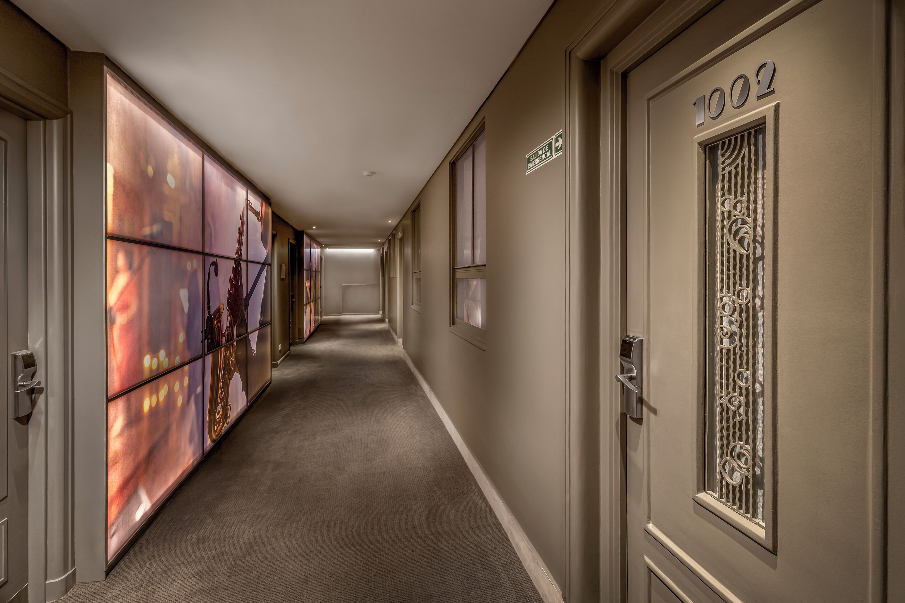 A hotel hallway with a carpeted floor, a door labeled "1002", and a wall with a decorative panel.